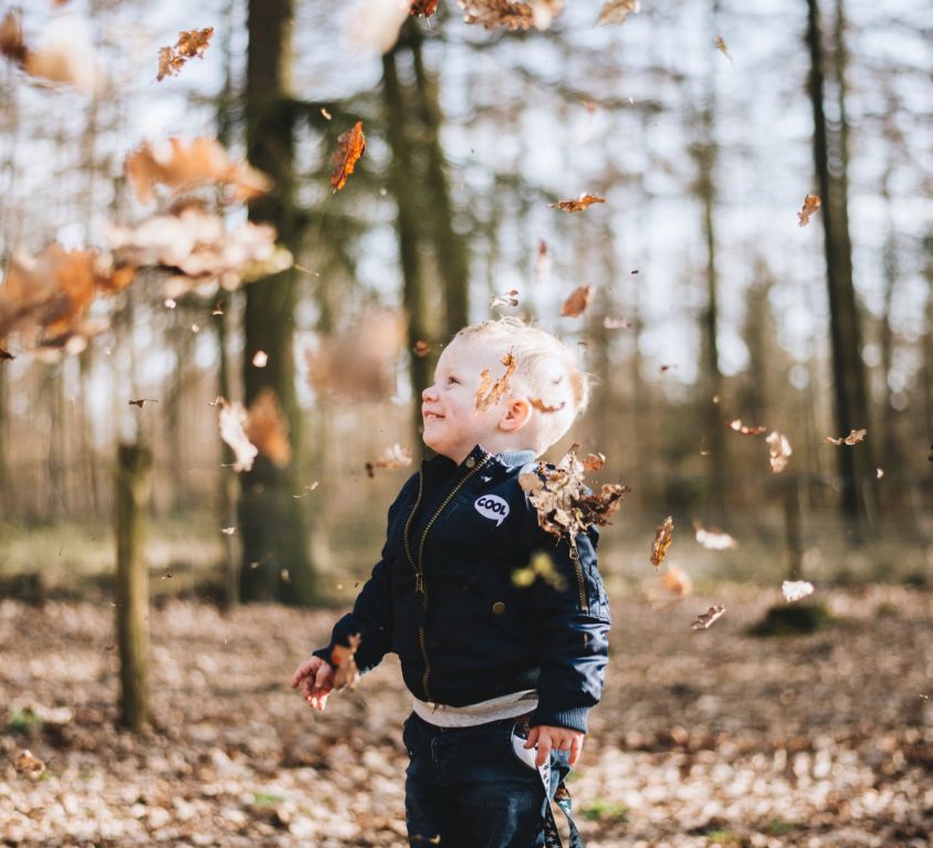 young boy laughing under falling leaves autumn perfectionism