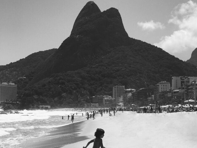 A black and white photo of a child running from the ocean on the sand with the dark silhouette of a hill in the background